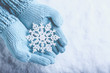 Female hands in light teal knitted mittens with sparkling wonderful snowflake on snow background. Winter and Christmas concept