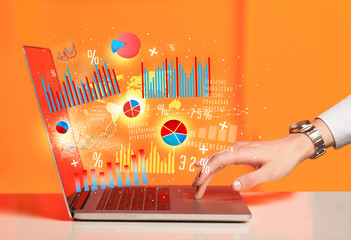 Hand typing on modern laptop notebook computer with graph icons