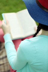 Wall Mural - Young woman with book sitting on green grass outdoors