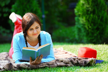 Wall Mural - Young woman with book lying on green grass outdoors