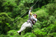 A group of people in climbing gear zip lining through the forest canopy on a wire suspended high above the jungle floor.