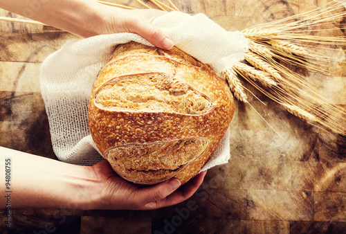 Fotografie, Obraz Baker holding a loaf of bread on rustic bacgkround