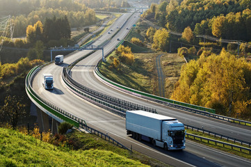 Wall Mural - Asphalt highway with electronic toll gates in autumn woodland. Three trucks on the road. The bridge spanning the valley. View from above. Sunny day with bright fall colors.