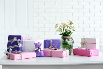 Poster - Composition of colourful gift boxes and flowers in glass on white table in front of brick wall background