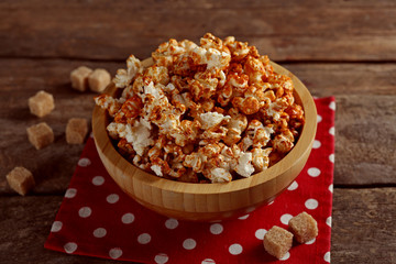 Wall Mural - Sweet caramel popcorn in a bowl on red cotton napkin against wooden background