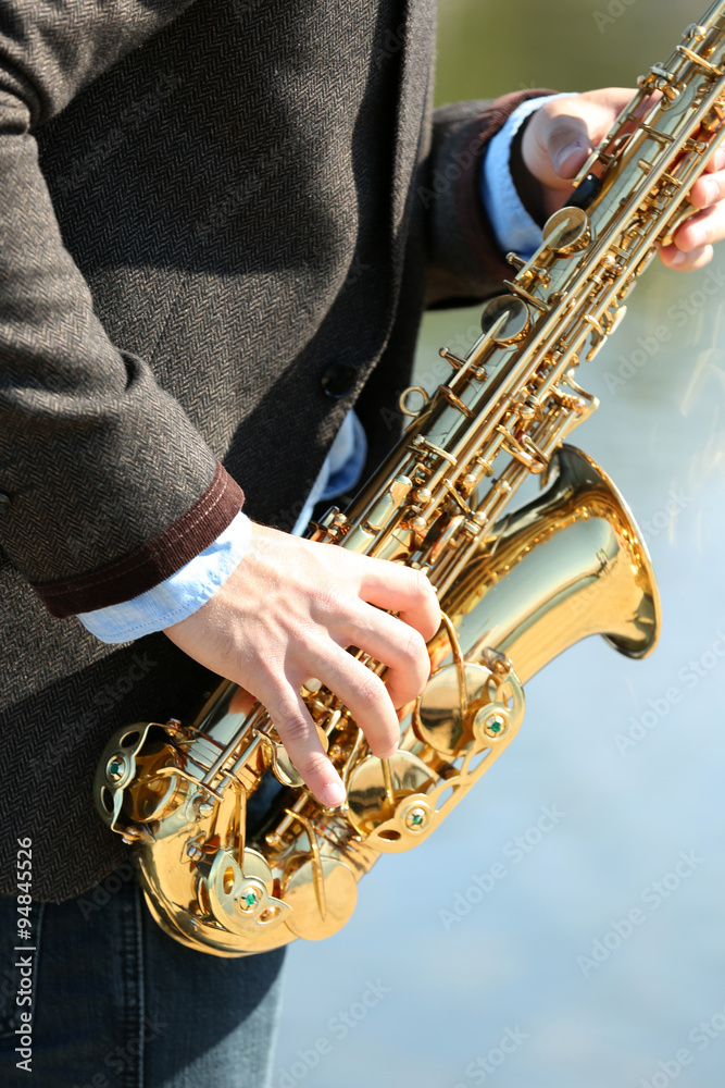 Young man playing on saxophone on the riverside