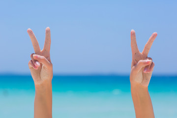 Female hands showing victory sign on blue sea background