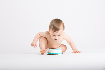 a cute 1 year old sits in a white studio setting. The boy in the middle of the shot about to get another face full of cake. He is only dressed in a white diaper