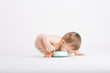 © revelpix - a cute 1 year old sits in a white studio setting. The boy takes a huge bite of cake on the floor with his face.. He is only dressed in a white diaper