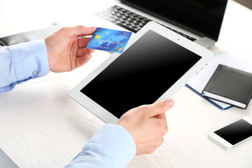 Wall Mural - Man holding credit card and tablet on workplace background