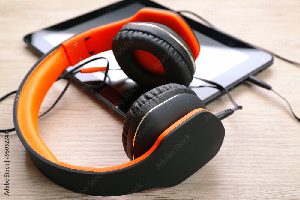 Headphones with tablet on wooden table close up