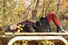 Beautiful Girl Lying On The Bench In Park Colored In Autumn Colo