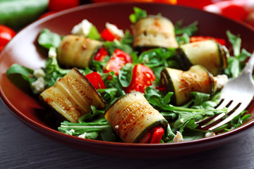 Wall Mural - Salad with arugula and zucchini rolls on plate, on table background