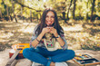 © kegfire - Smiling caucasian teen hipster girl sitting outdoors with guitar. Creative artistic young woman wearing casual clothes having a picnic with cupcake on autumn day.