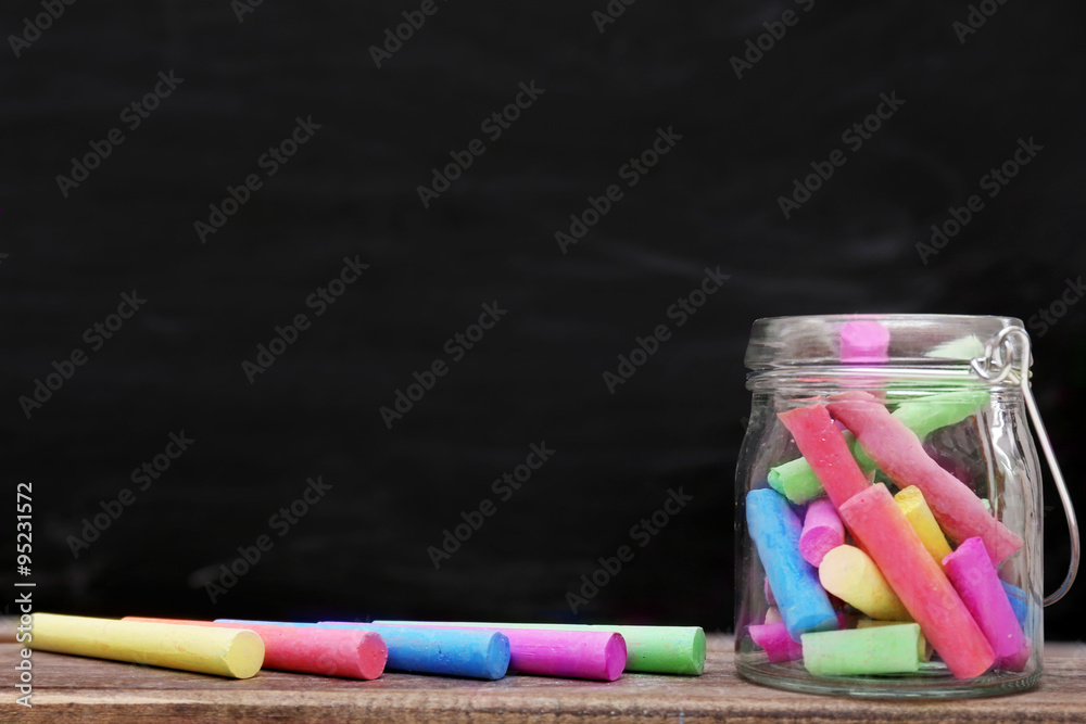 Multicoloured chalk in a jar on blackboard background