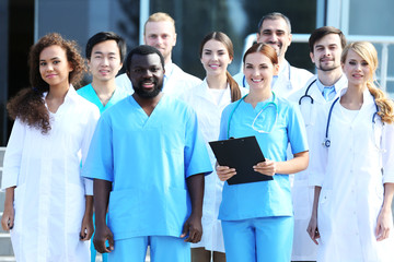 Wall Mural - Smiling team of young doctors against hospital entrance