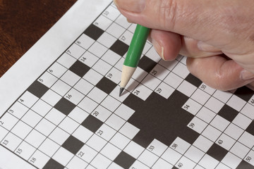 An elderly woman is doing crossword puzzle. It is a good exercise for brains especially for older people. It is a relaxing habit to spend some time alone.