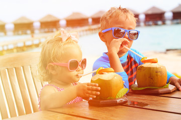 Wall Mural - little boy and toddler girl drinking coconut cocktail on beach resort