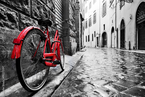 Fototapeta na wymiar Retro vintage red bike on cobblestone street in the old town. Color in black and white