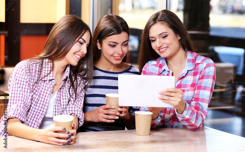 Three smiling friends with coffee looking at tablet