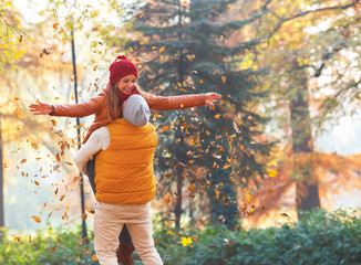 Smiling couple throwing leaves and having fun in autumn park, man carries woman in his hands.