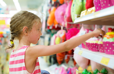 Little girl selecting toy on shelves in supermarket.