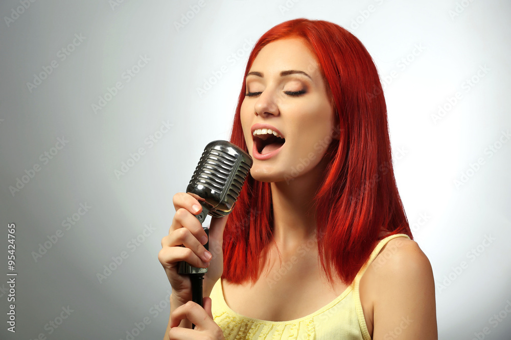 Beautiful young woman with microphone on gray background