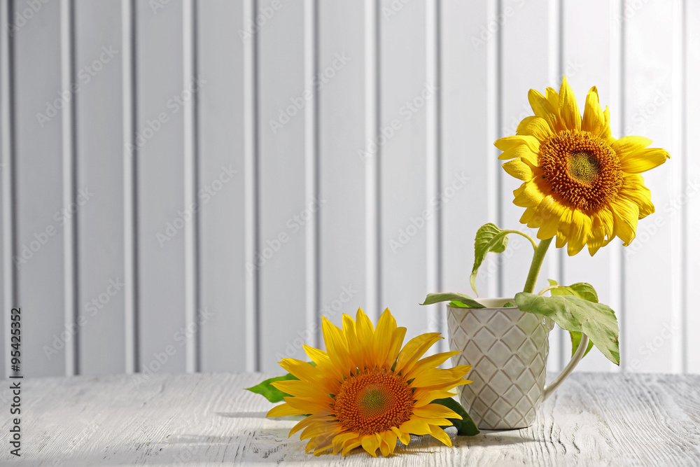 Beautiful bright sunflowers in cup on wooden background