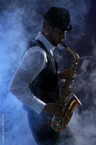 Fotografía Elegant saxophonist plays jazz on dark background in blue smoke