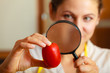 Woman inspecting tomato with magnifying glass.
