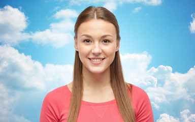 smiling young woman or teenage girl over blue sky