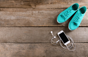 Poster - White cellphone with headphones and gumshoes on varnished wooden background