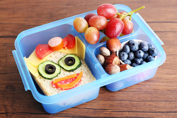 Wall Mural - Creative sandwich with fruits and nuts in lunchbox on wooden background