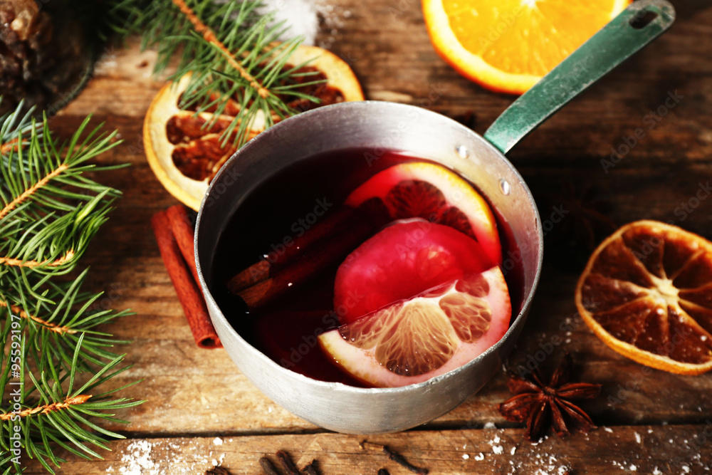 Mulled wine in stew-pan on decorated wooden background