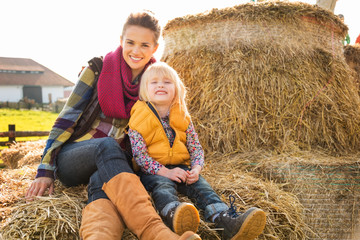 Wall Mural - Portrait of happy woman with cute child sitting on hay on farm
