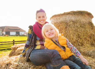 Wall Mural - Portrait of beautiful woman and cute girl sitting on hay on farm
