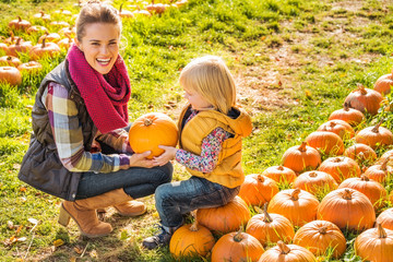 Wall Mural - Smiling woman and child choosing a pumpkin on farm