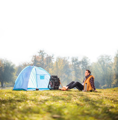 Wall Mural - Relaxed hiker sitting next to a blue tent