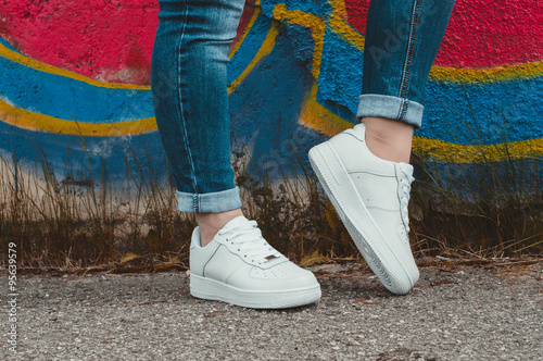 Fotografía White sneakers on girl legs on the graffiti background