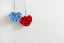 Two Hand Made Crochet Knit Hearts. Red Heart And Blue Heart Hanging On Threads. Neutral Textured Background. Valentines Day, Wedding Composition With Hearts.