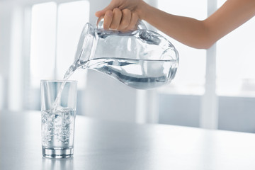 Wall Mural - Drink Water. Woman's Hand Pouring Water From Pitcher Into A Glass. Healthy Lifestyle.