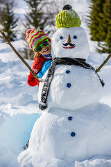 Wall Mural -  Christmas, Winter holiday, happy girl playing with snowman
