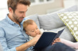 © goodluz - Father and child reading book in sofa