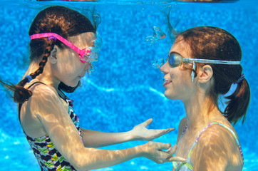 Children swim in pool underwater, happy active girls in goggles have fun in water, kids sport on family vacation
