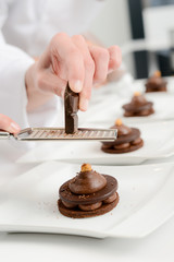 close up of professional pastry cook hands preparing chocolate dessert in restaurant kitchen