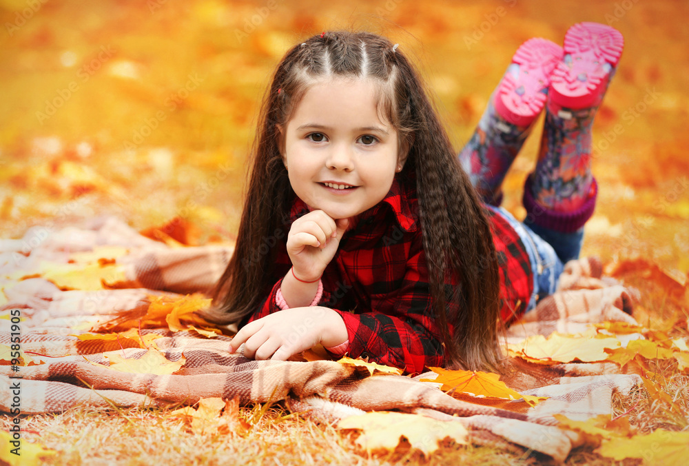 Happy young girl lying on plaid in autumn park