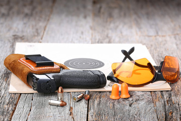 Automatic Handgun with leather holster, bullets and safety glasses on a wooden background.