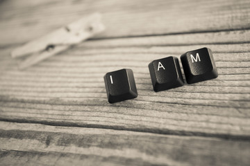 I AM wrote with keyboard keys on wooden background, black and wh