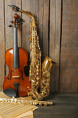 Canvas Print - Musical instruments: saxophone, violin and flute with notes on wooden background