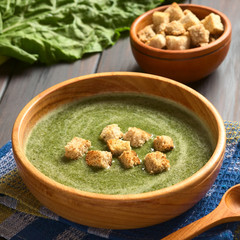 Canvas Print - Cream of chard soup with croutons in wooden bowl, photographed on dark wood with natural light (Selective Focus, Focus on the first croutons)
